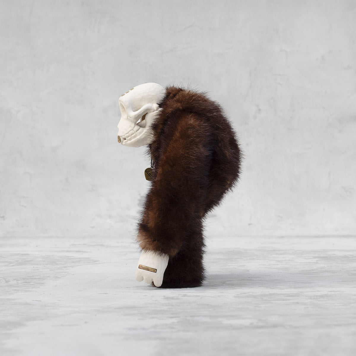 Side view of a ceramic, fur, and brass monkey skull figurine standing against a light gray background