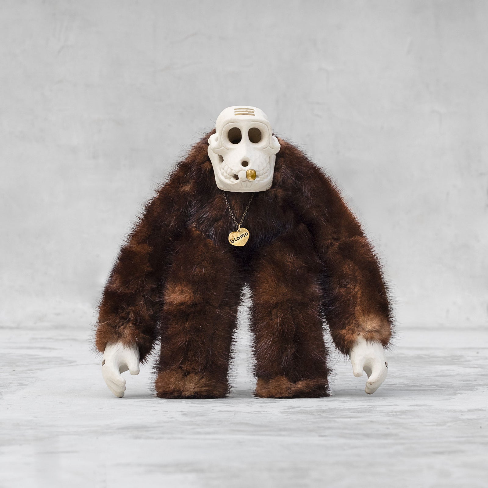 Ceramic, fur, and brass monkey skull figurine standing against a light gray background