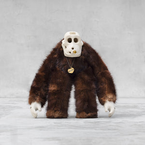 Ceramic, fur, and brass monkey skull figurine standing against a light gray background