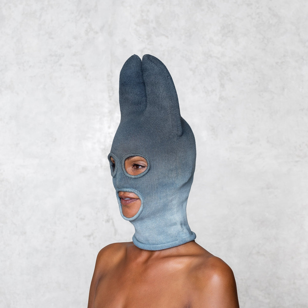 A woman from the shoulders up wearing a cotton Knit Bat balaclava in faded indigo