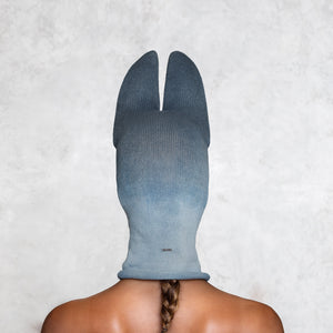 A woman from the shoulders up facing back wearing a cotton Knit Bat balaclava in faded indigo