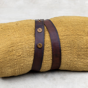 Brown leather belt with copper buttons displayed on a mango colored blanket wrap