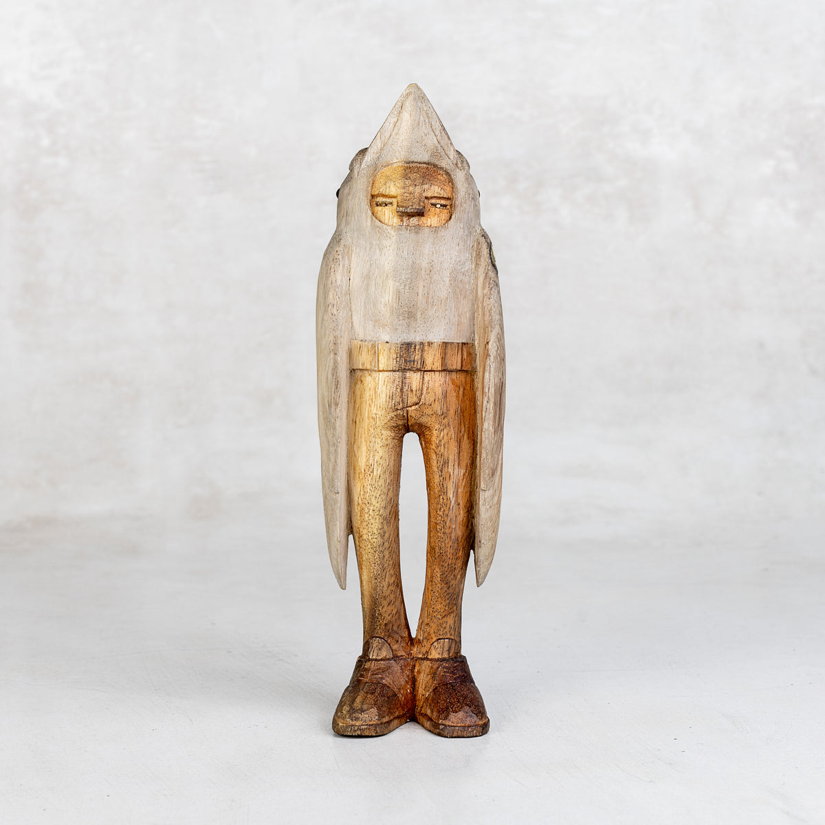 Wooden sculpture of a figure with a beak hood and wing arms on a white background