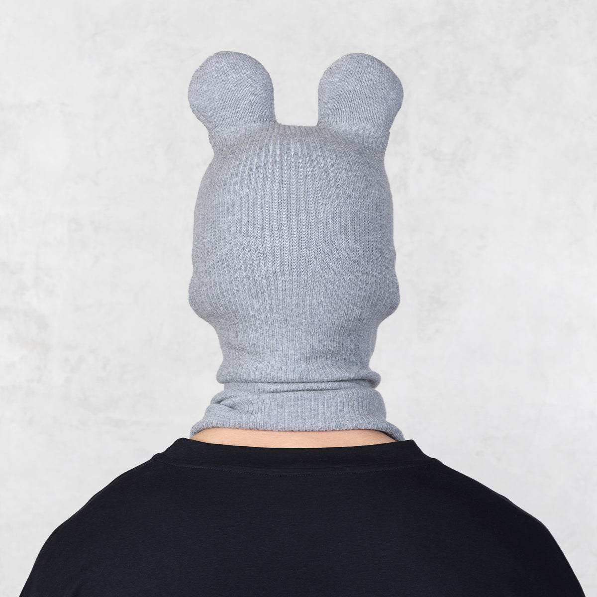 Person wearing a gray knitted hood with ears on a light gray background