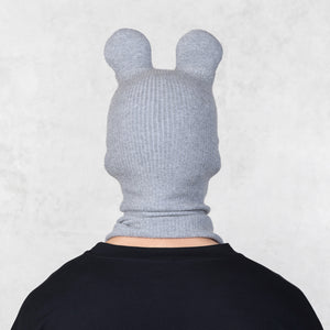 Person wearing a gray knitted hood with ears on a light gray background