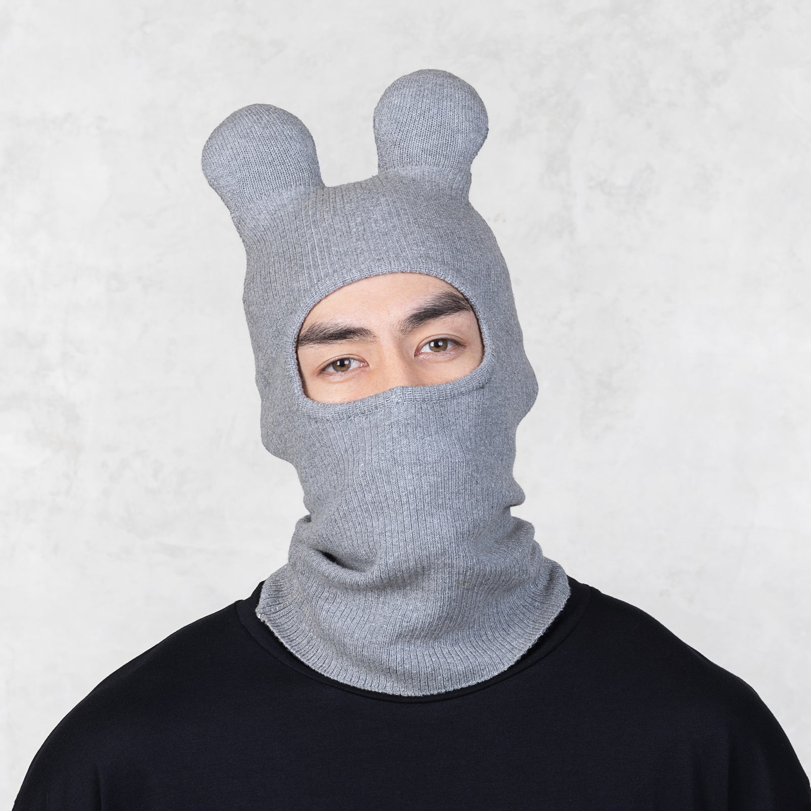 Person wearing a gray knit balaclava with animal ears on a light gray background