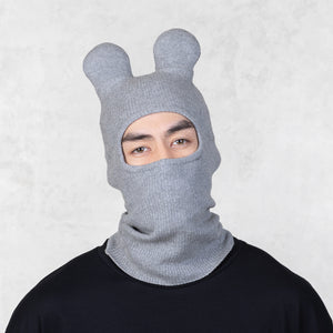 Person wearing a gray knit balaclava with animal ears on a light gray background