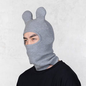 Person wearing a gray knit balaclava with bunny ears on a light gray background