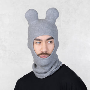 Person wearing a gray knit balaclava with bear ears on a light gray background