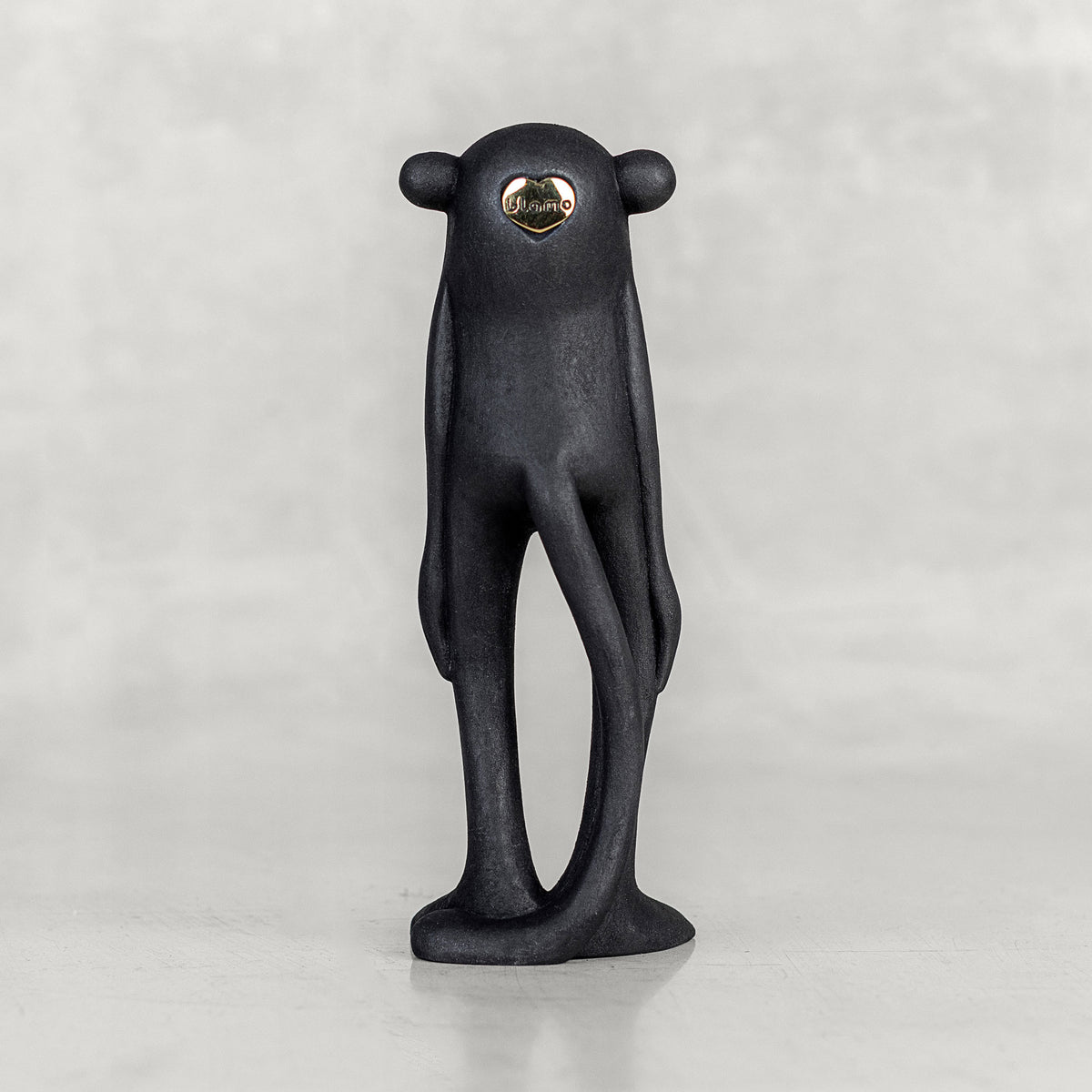 Back view of a black monkey figurine with a brass emblem on a white background