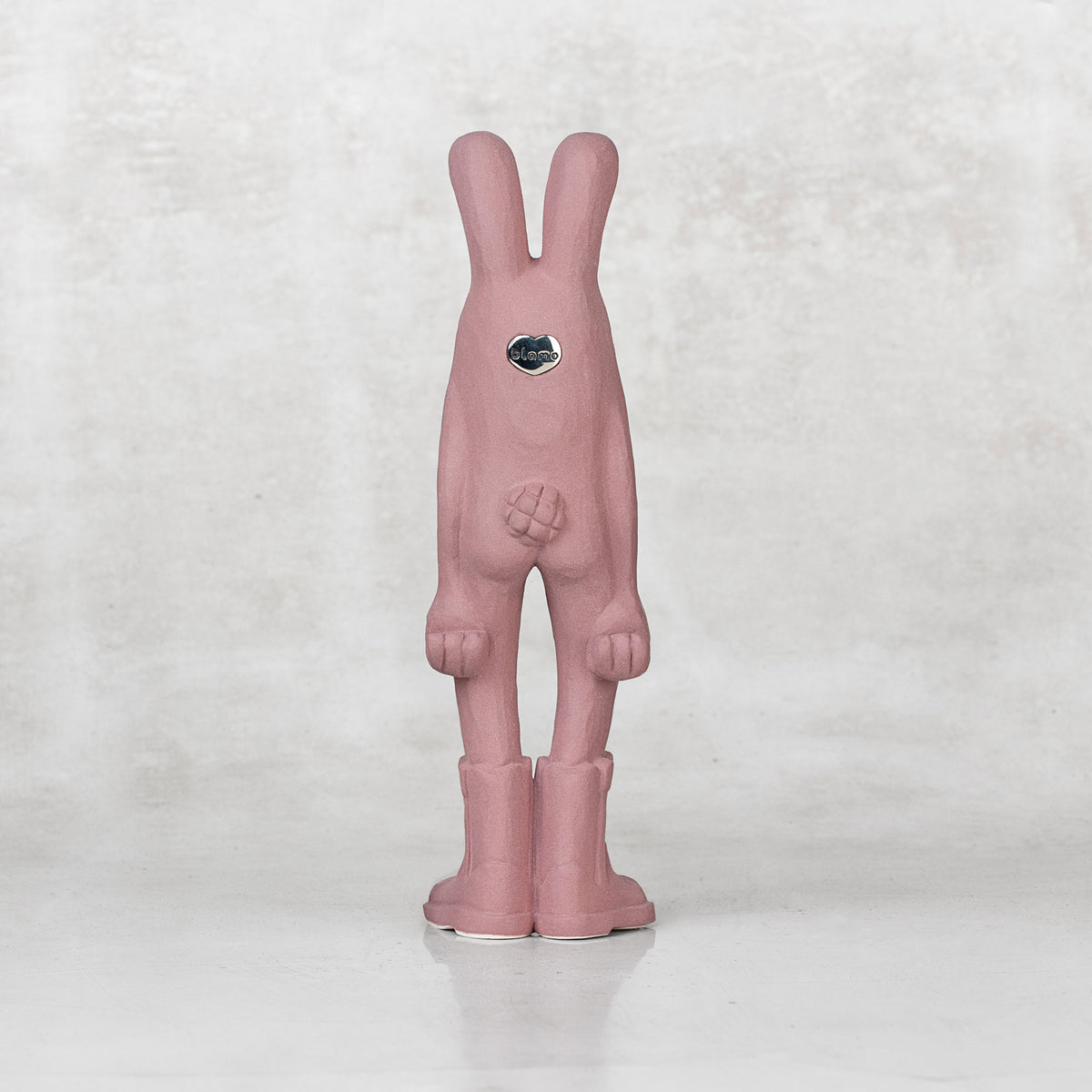 Back view of a ceramic lavender bunny statuette against a light gray background