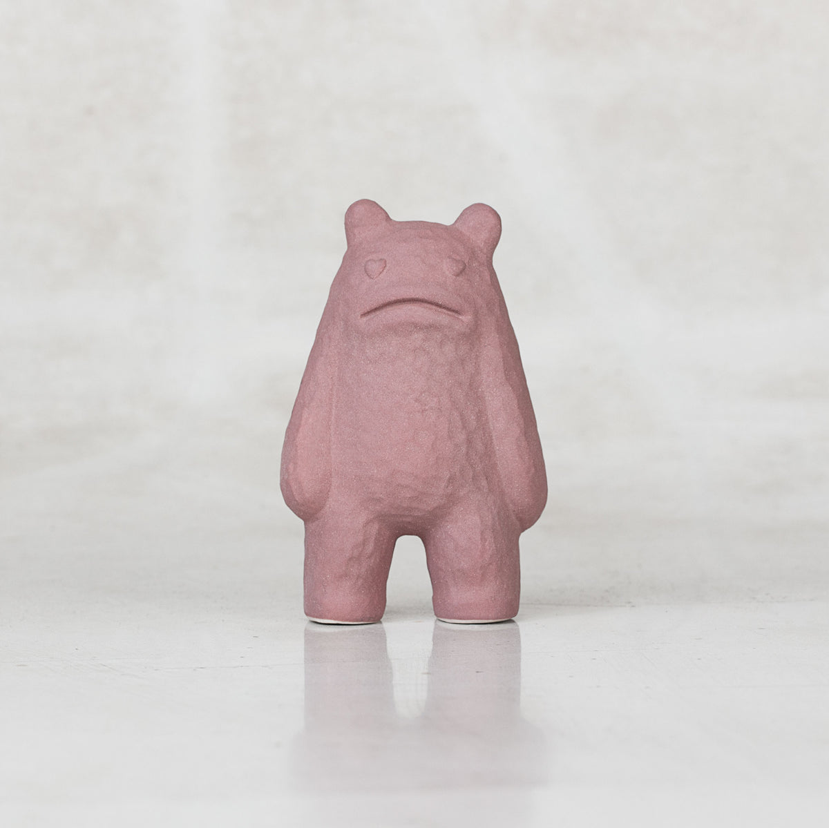 Ceramic lavender creatures with heart eyes frowning against a light gray background