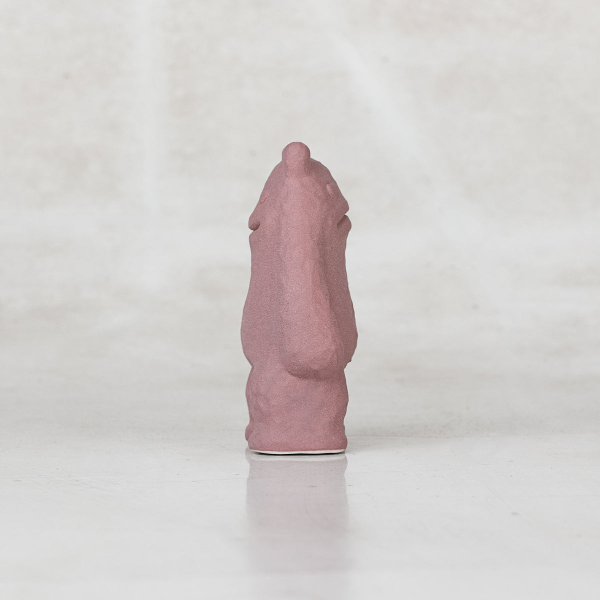 Side view of a ceramic lavender creature with faces on the front and back side of its head against a light gray background