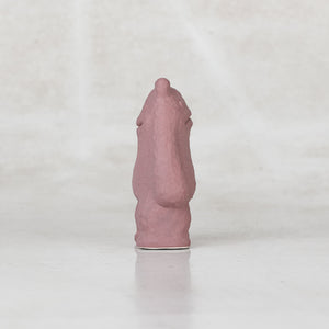 Side view of a ceramic lavender creature with faces on the front and back side of its head against a light gray background