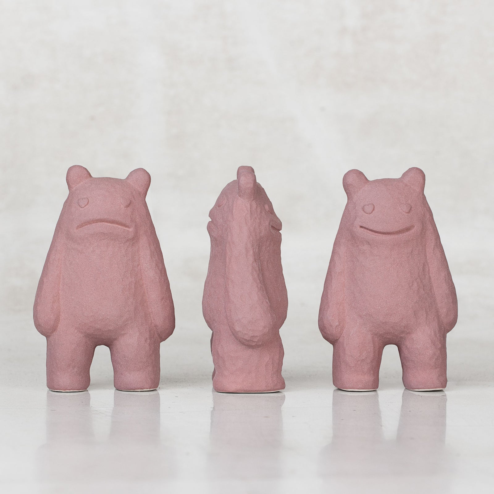 3 Ceramic lavender creatures with faces on the front and back sides of their heads facing different directions against a light gray background