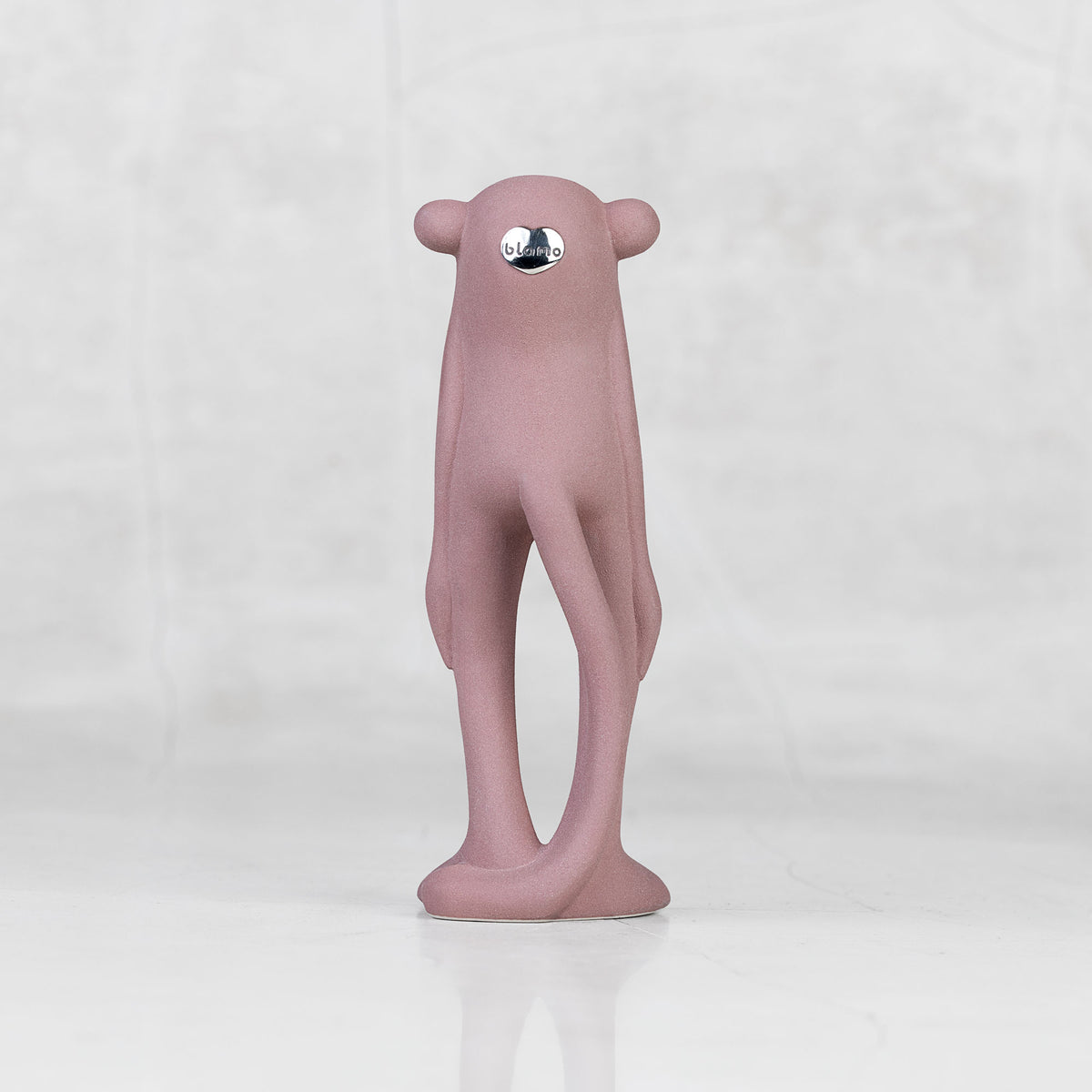 Back view of a lavender ceramic monkey statuette against a light gray background