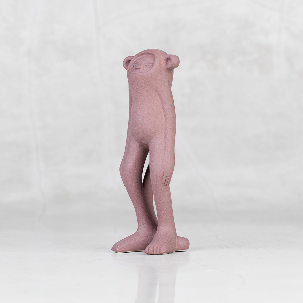 Quarter view of a lavender ceramic monkey statuette with brass eyes against a light gray background