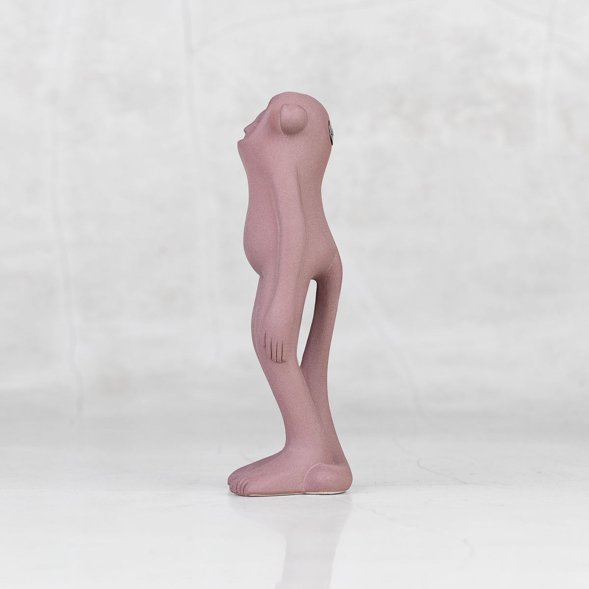 Side view of a lavender ceramic monkey statuette with brass eyes against a light gray background