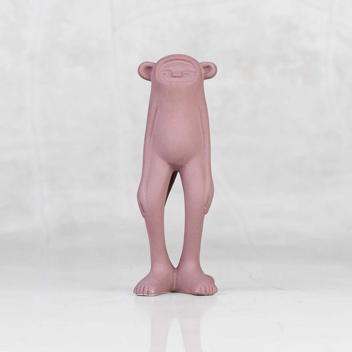 Lavender ceramic monkey statuette with brass eyes against a light gray background