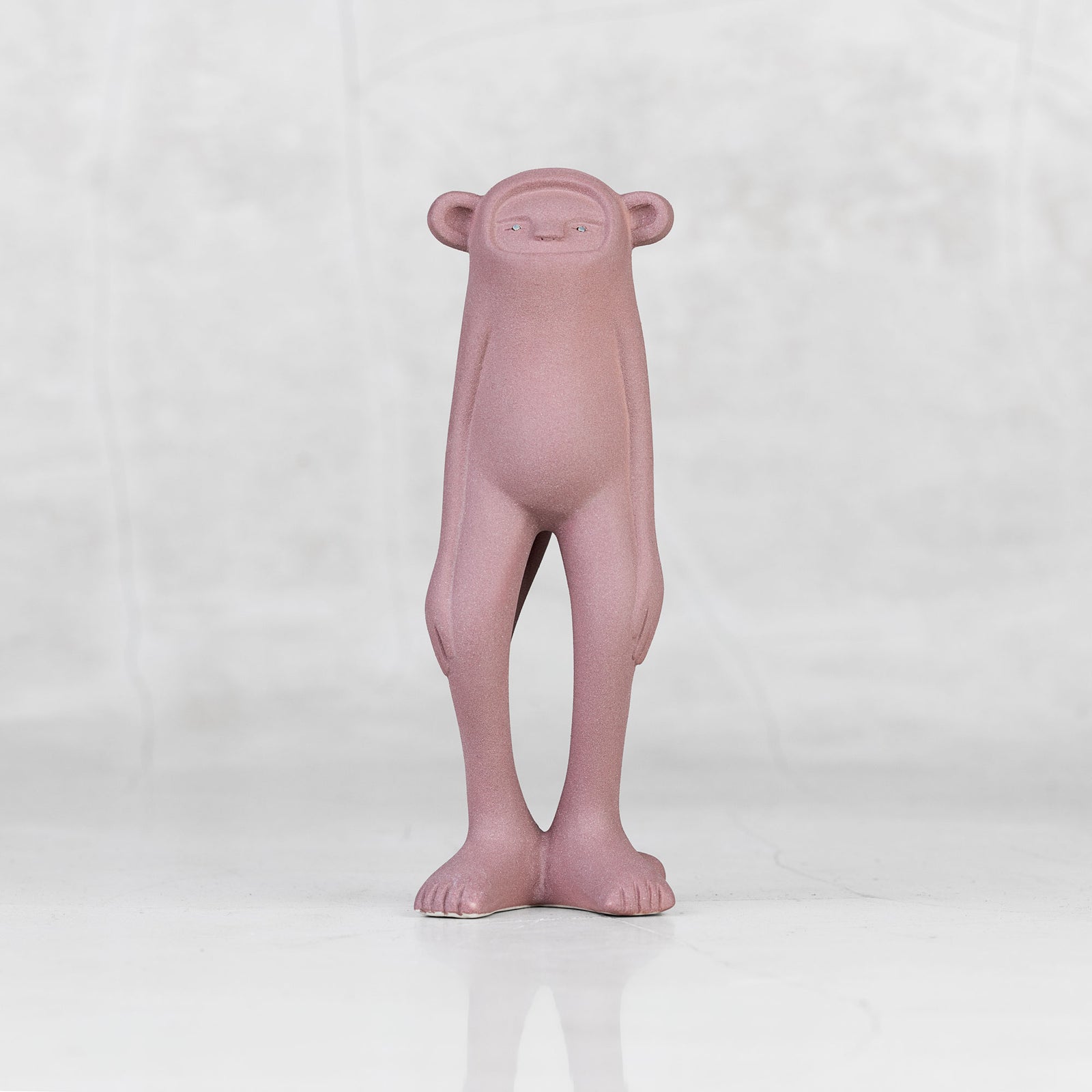 Lavender ceramic monkey statuette with brass eyes against a light gray background