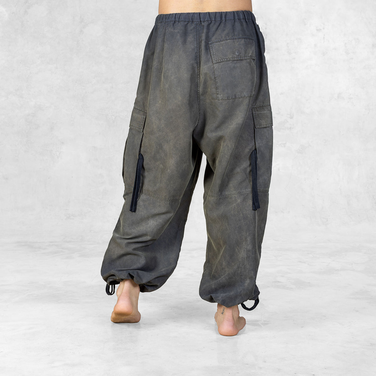 Person from the feet to the waist facing back wearing hand painted olive oversized raver-style pants on a white background