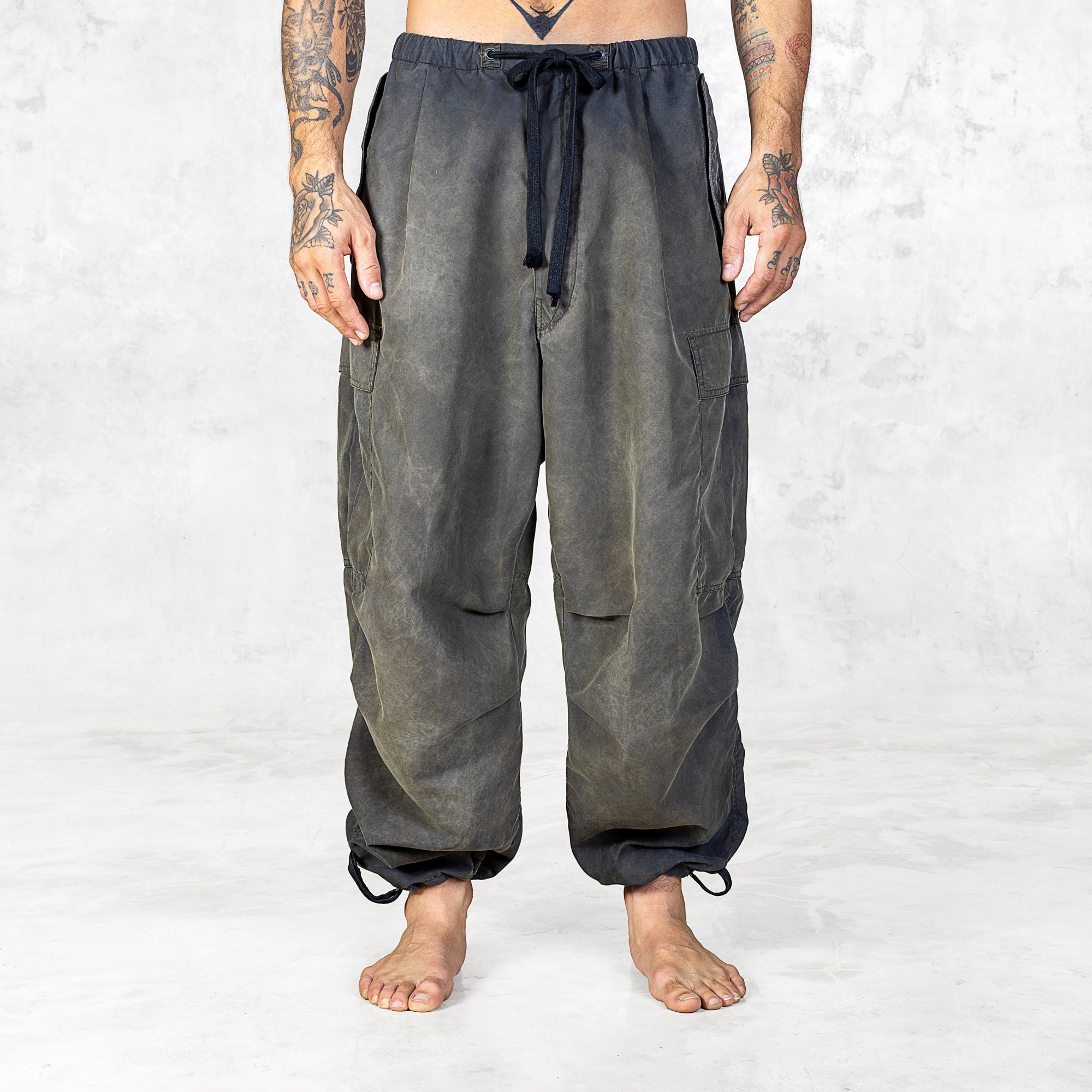 Person from the feet to the waist wearing hand painted olive oversized raver-style pants on a white background