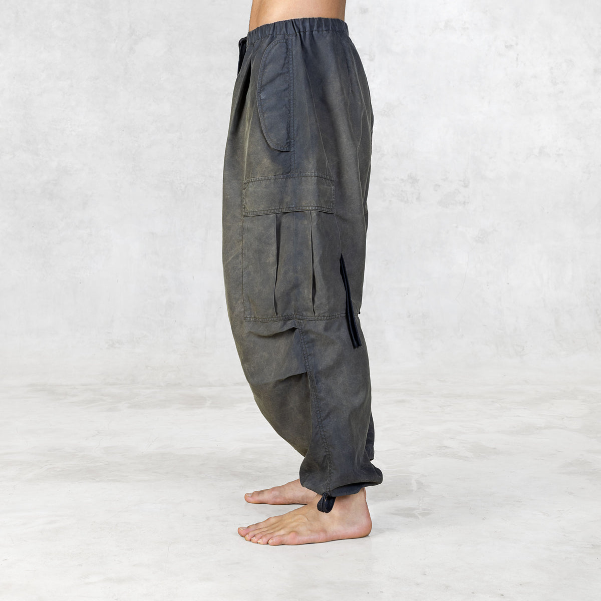 Person from the feet to the waist facing side wearing hand painted olive oversized raver-style pants on a white background