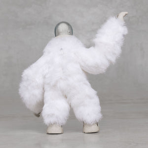 White furry creature statue with its arm raised against a light gray background 