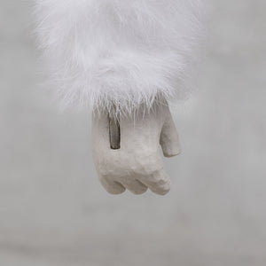 White furry arm and ceramic and brass hand on a light gray background