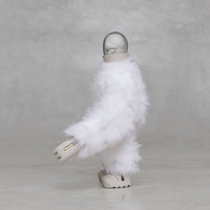 Side view of a white furry creature statue against a light gray background 