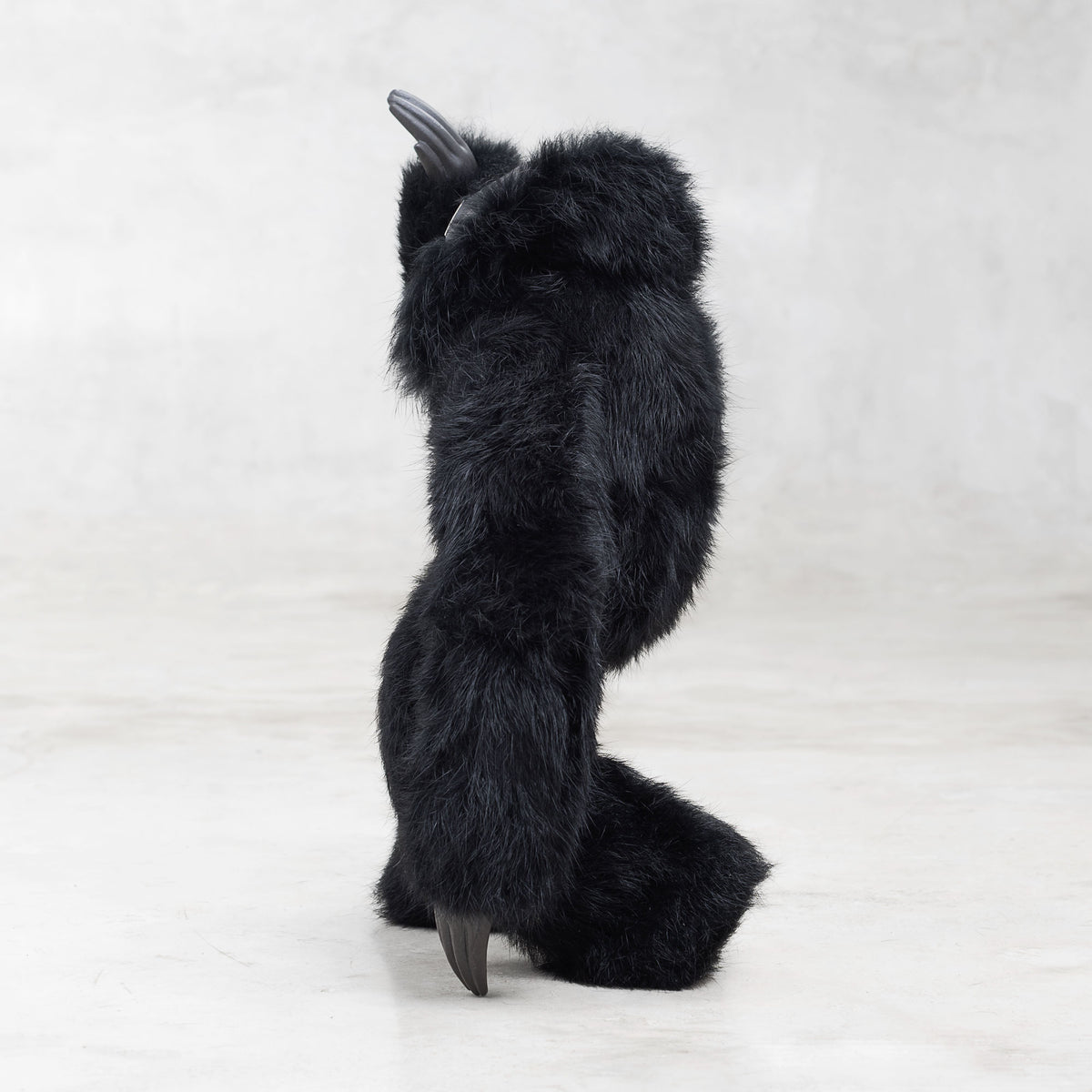 Side view of a black furry creature with one arm raised on a light gray background