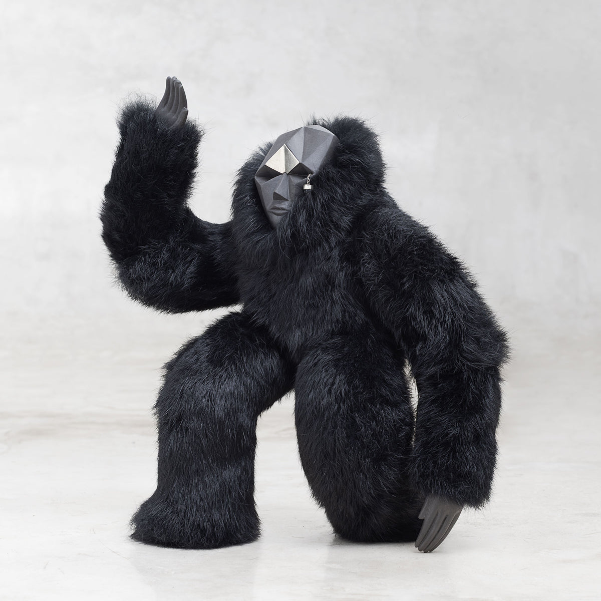 Ceramic, fur, and white brass creature figurine sculpture with one arm raised in the air standing against a light gray background