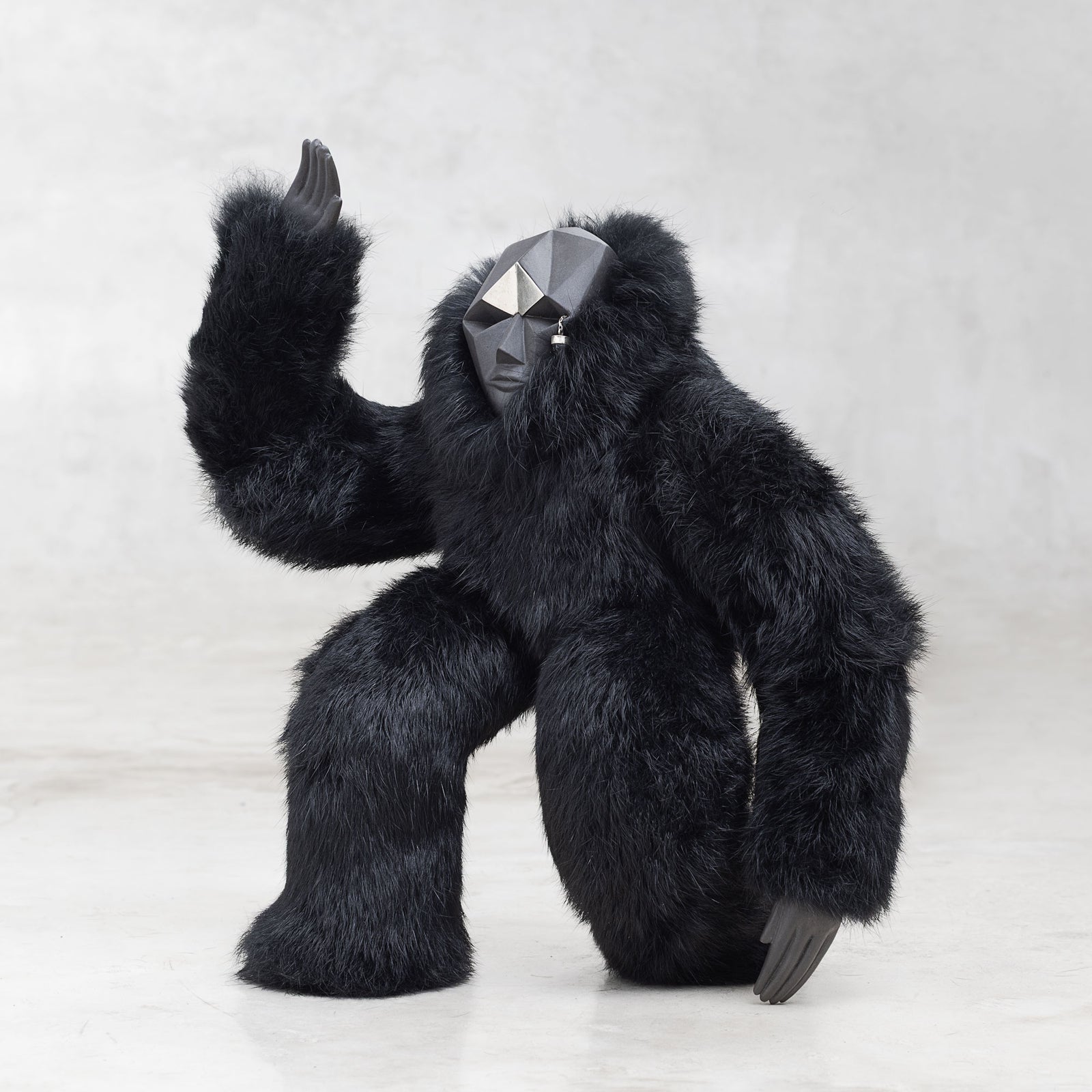 Ceramic, fur, and white brass creature figurine sculpture with one arm raised in the air standing against a light gray background