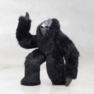 Ceramic, fur, and white brass creature figurine sculpture with one arm raised in the air standing against a light gray background