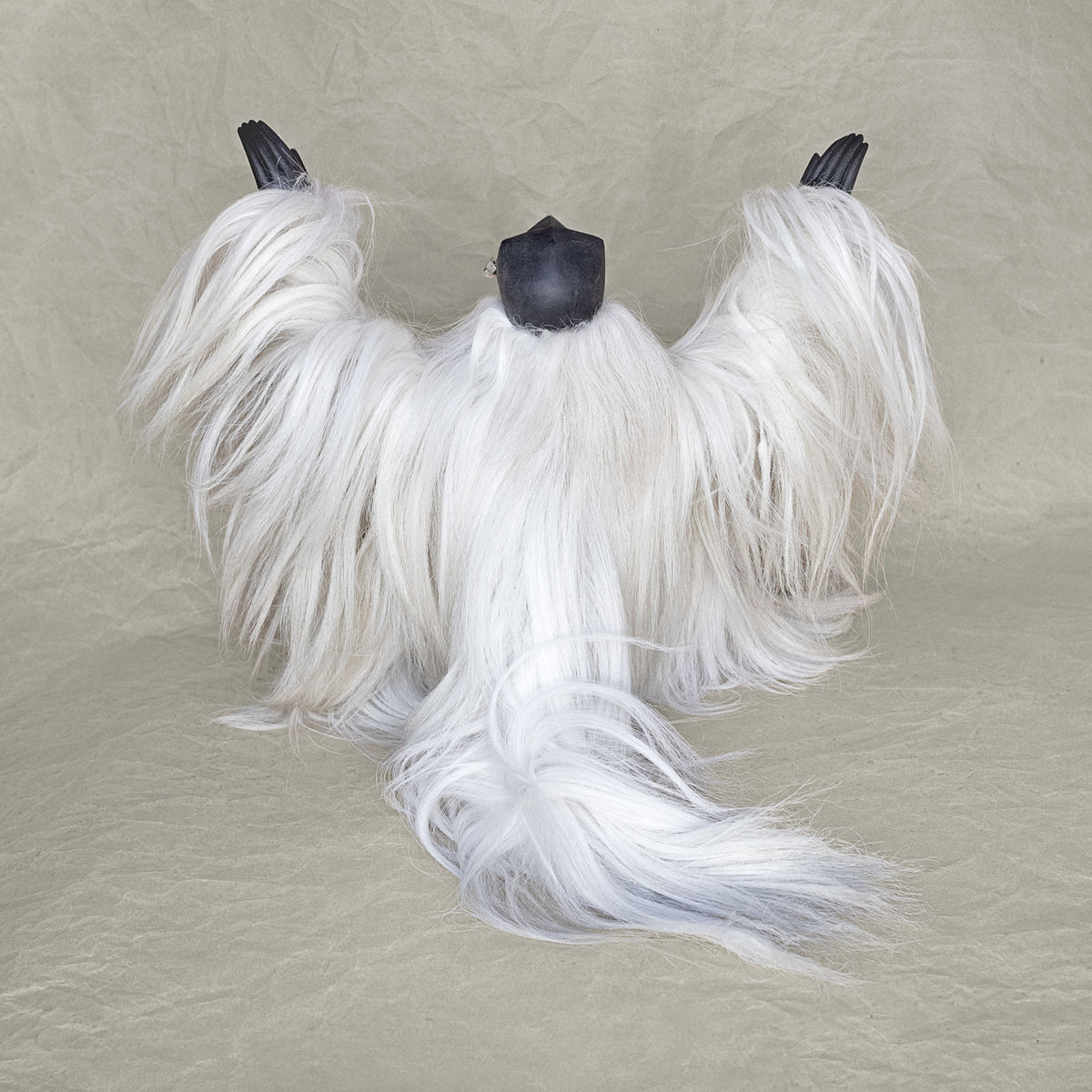 Back view of a ceramic fur creature sculpture with its arms raised above its head standing against a beige background