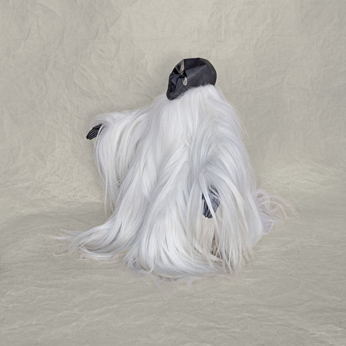Side view of a ceramic fur and brass creature sculpture standing against a beige background