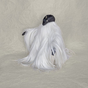 Side view of a ceramic fur and brass creature sculpture standing against a beige background
