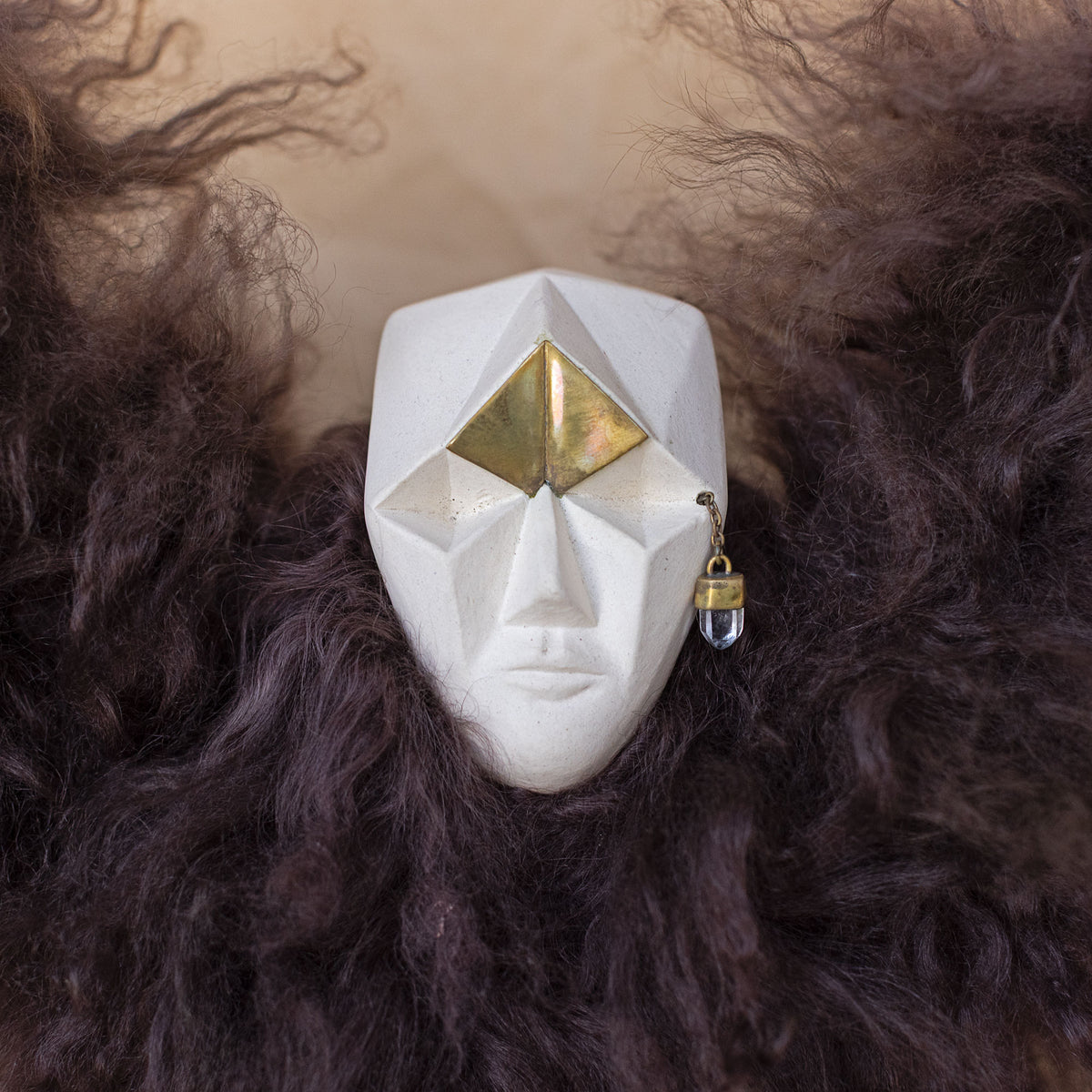 Closeup of a creature sculpture made of ceramic, fur, and brass against a beige background