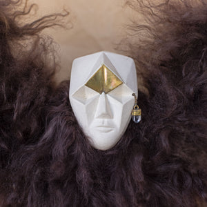Closeup of a creature sculpture made of ceramic, fur, and brass against a beige background