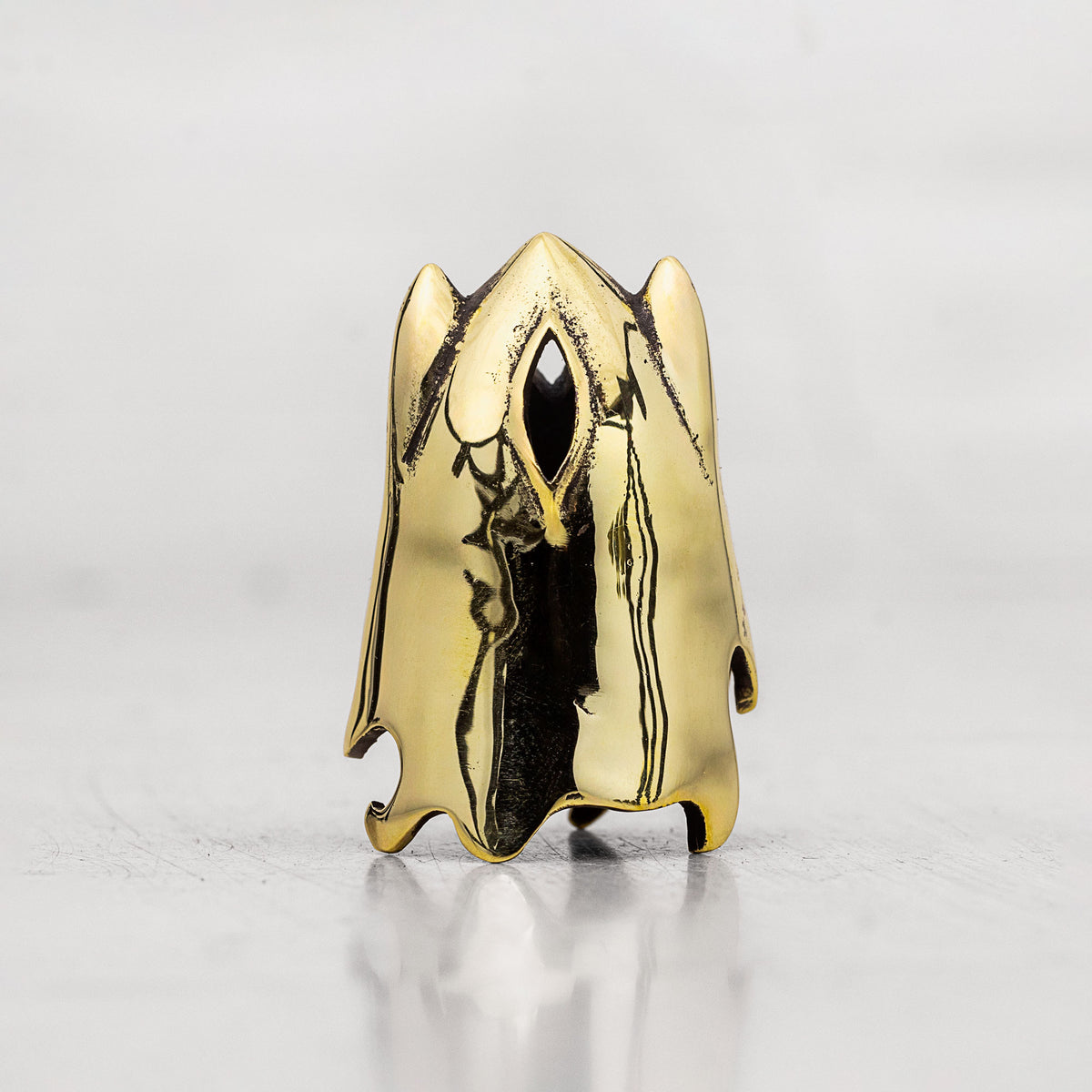 A gold ghost-shaped thimble with a polished finish and a black eye detail, standing on a reflective light gray surface.