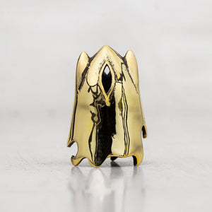 A gold ghost-shaped thimble with a polished finish and a black eye detail, standing on a reflective light gray surface.