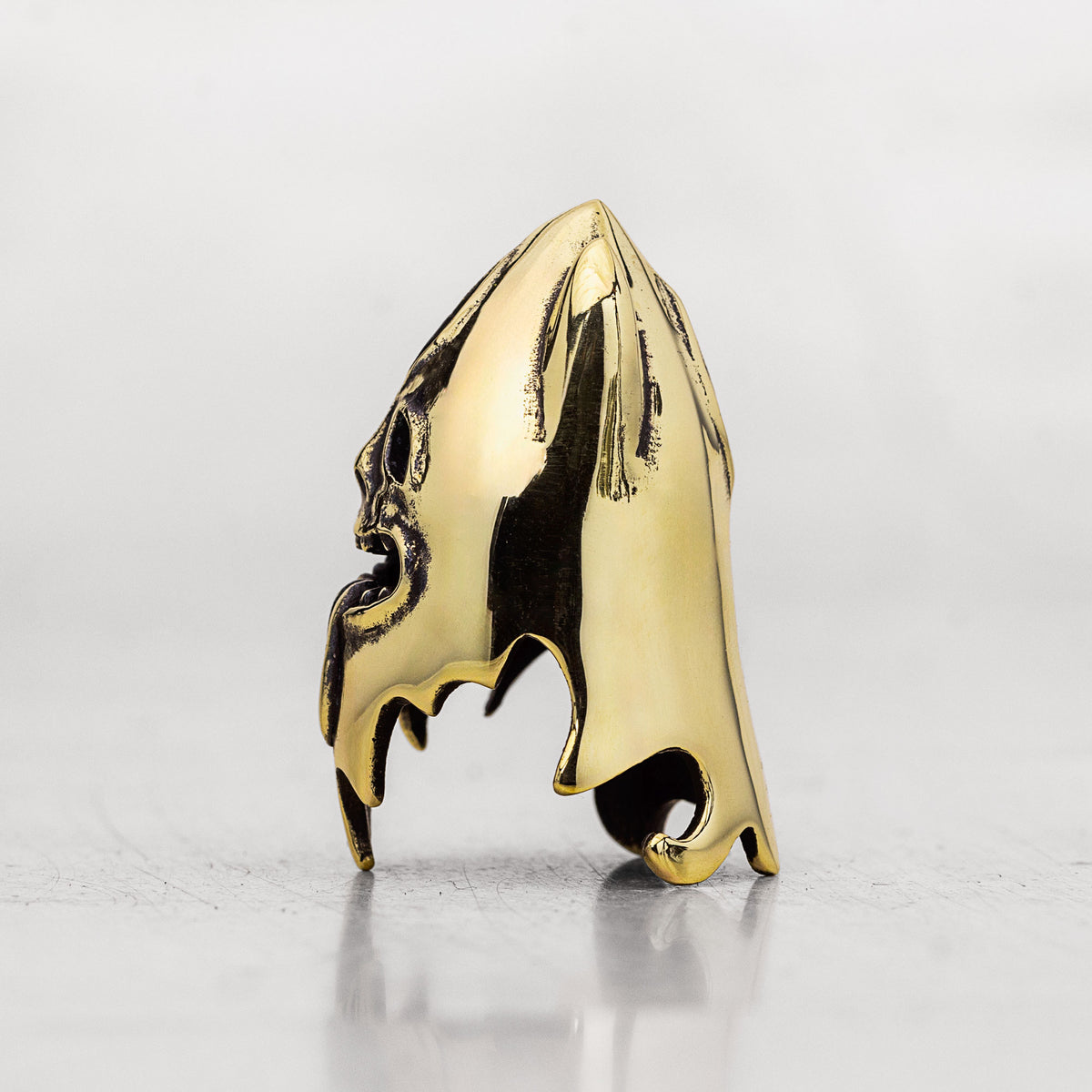 A polished gold thimble with a glossy finish, standing upright on a reflective gray surface against a light gray background.