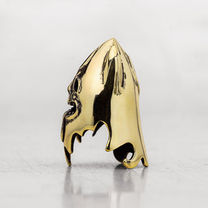 A polished gold thimble with a glossy finish, standing upright on a reflective gray surface against a light gray background.