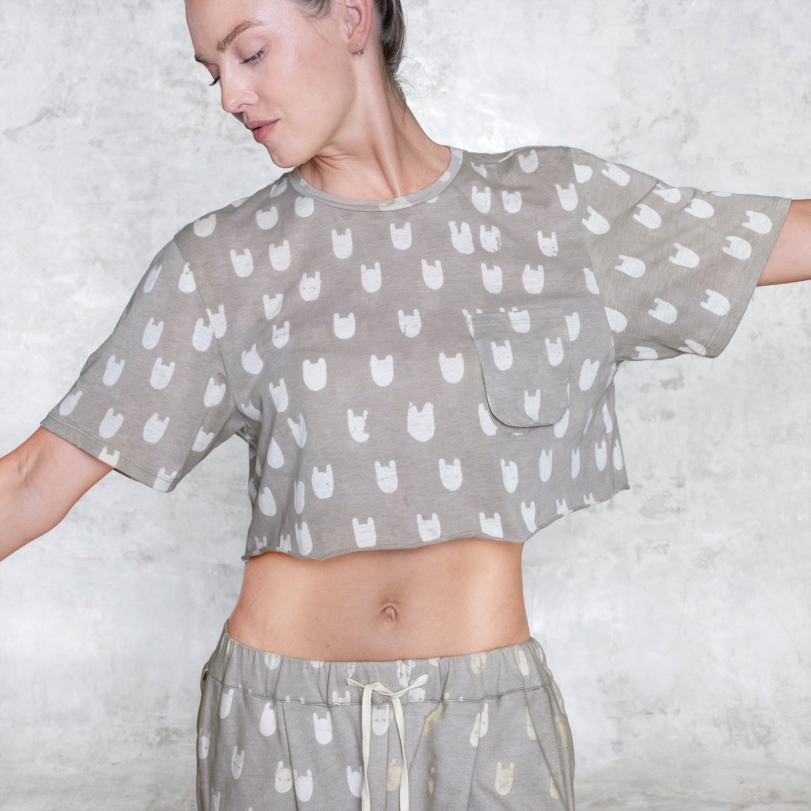 Person wearing a BLAMO Crop Batik Socky Tee Cream featuring a chest pocket   looking down with their arms outstretched against a light gray background 