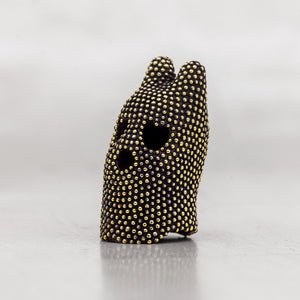 Black and gold brass object with two eye holes and a mouth hole on a light gray background