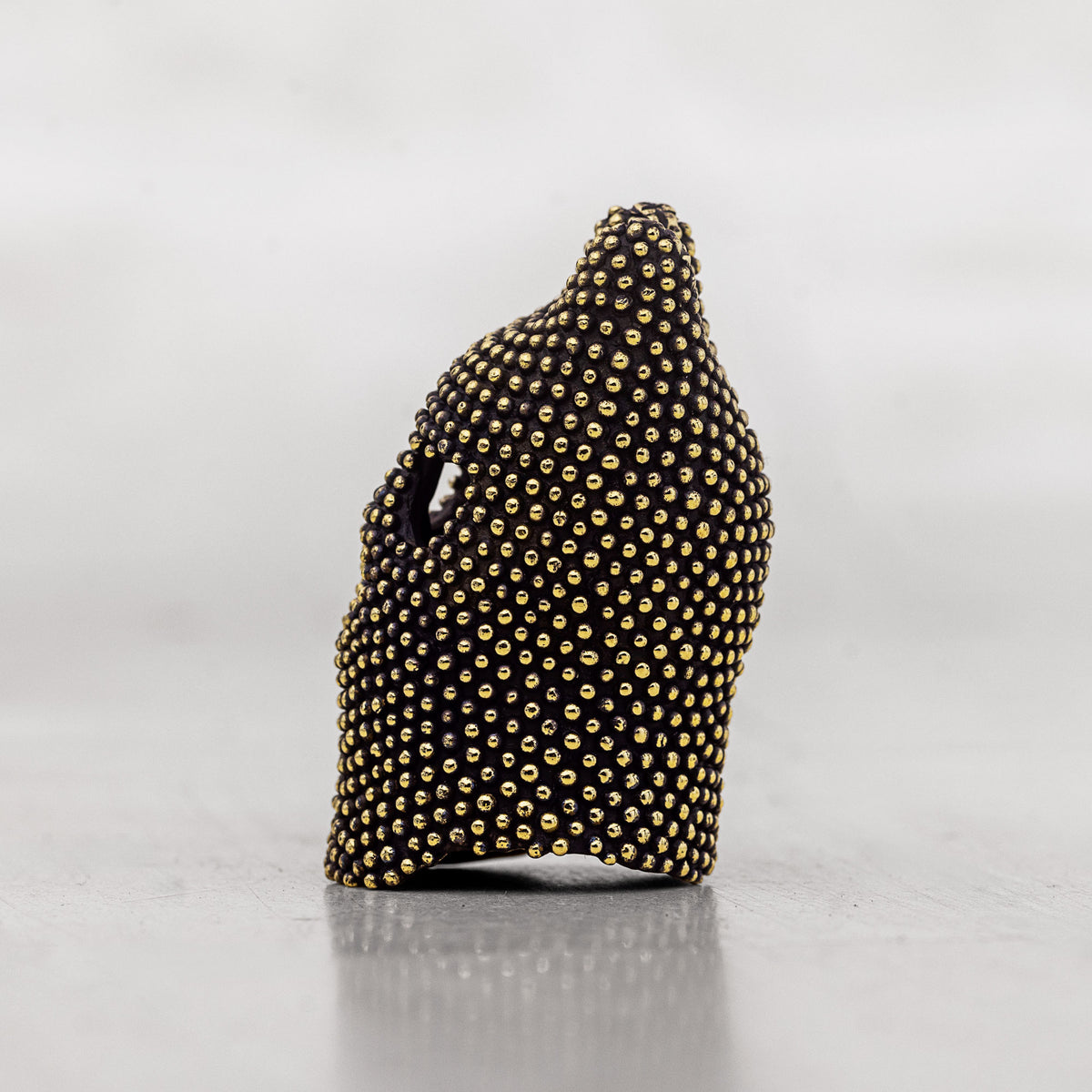Black with gold studs brass art piece on a white surface
