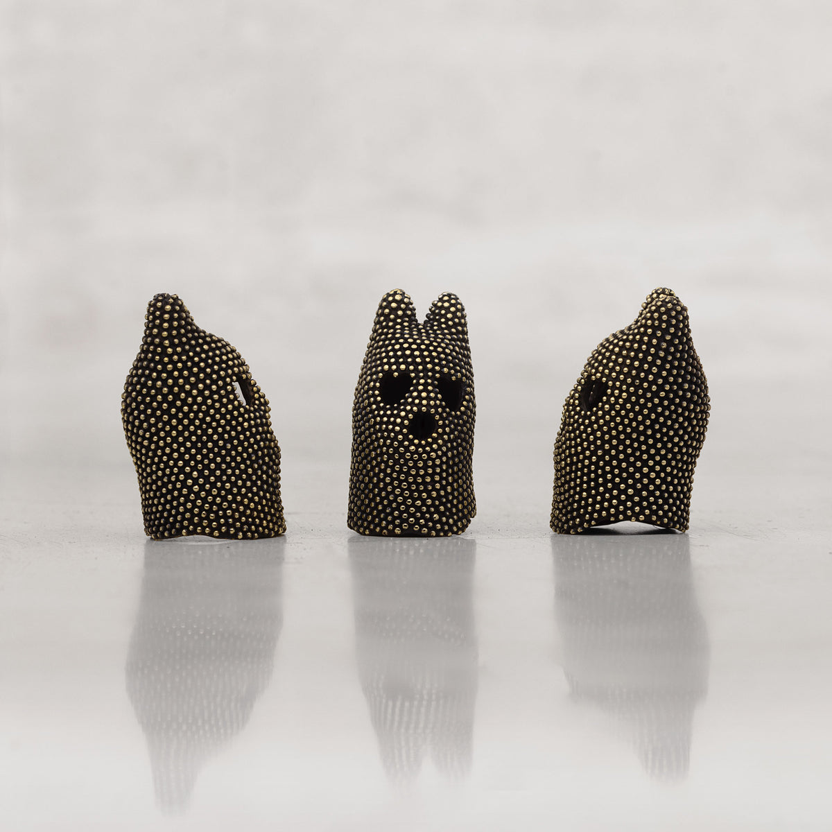 Three black and gold studded creature heads with cat-shaped ears on a white background