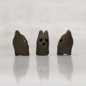 Three black and gold studded creature heads with cat-shaped ears on a white background