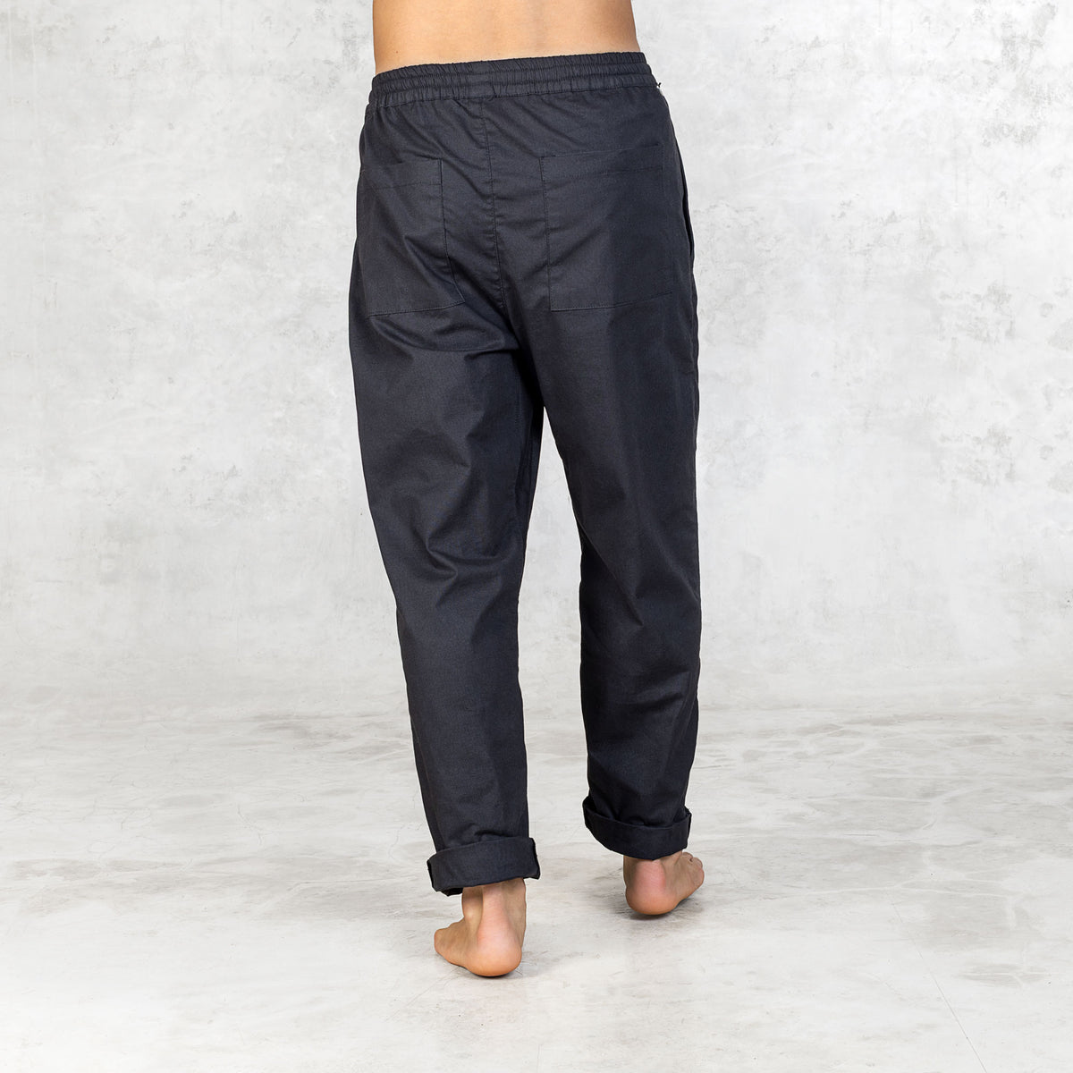 Person wearing Dagger Blamo pants, barefoot, shown from back view. The pants have a full elastic waist, drawstring, and front zipper pockets, with slightly tapered legs