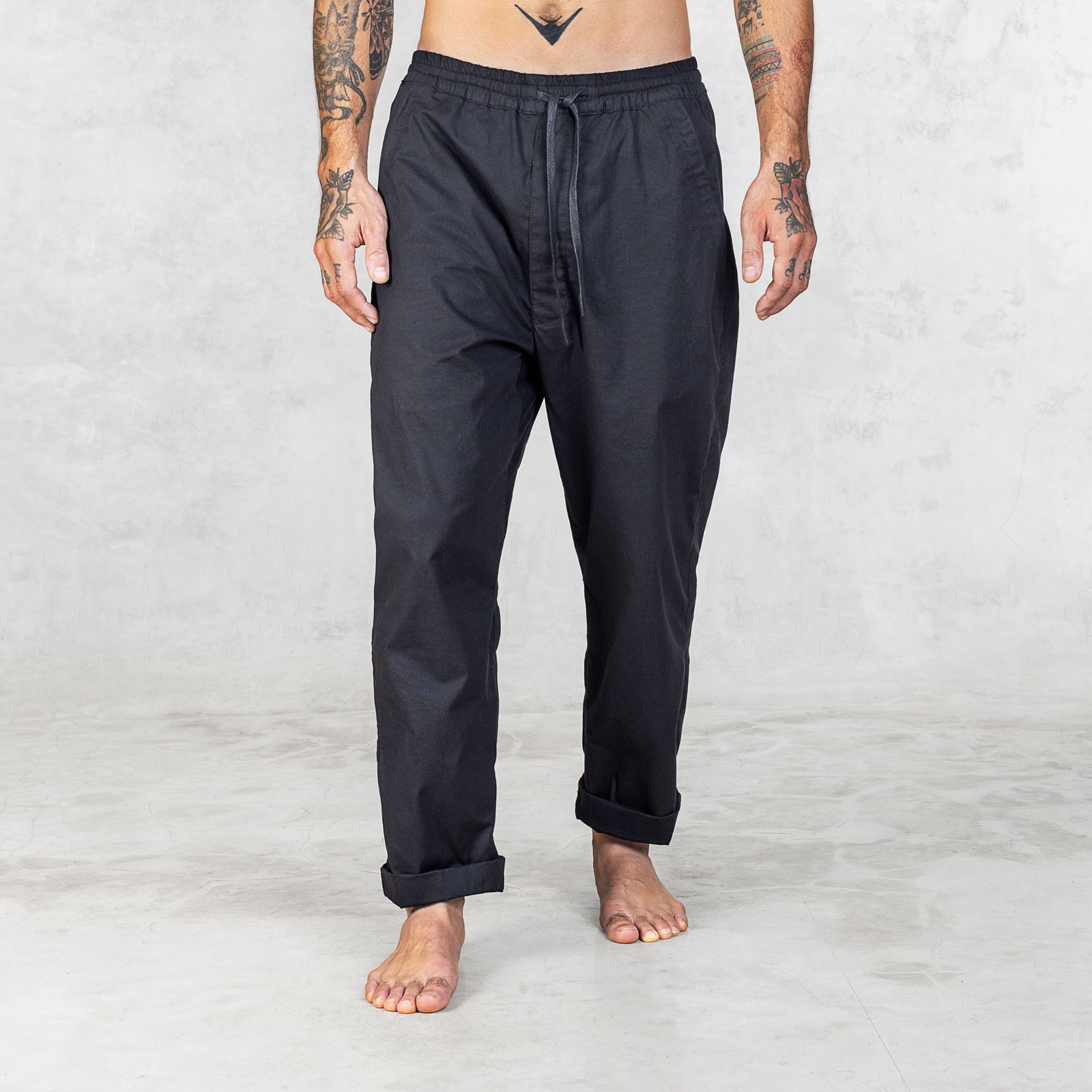 Person wearing Dagger Blamo pants, barefoot, shown from front view. The pants have a full elastic waist, drawstring, and front zipper pockets, with slightly tapered legs